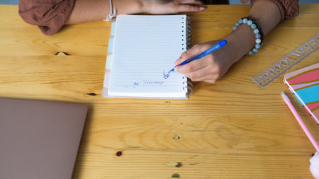 Close up of teenage girl hands doing homework while sitting at desk. She wrote date and title in...