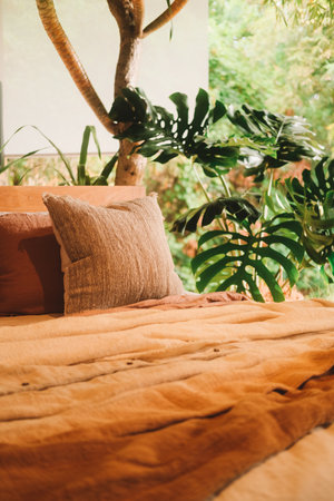 Tropical luxury bedroom. View of the bed next to which is a large window into the jungle, next to it is a monstera plant. On the bed are brown natural bed linen. Eco-friendly design.の写真素材