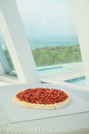 A festive wedding cake Pavlova decorated with fresh strawberries and raspberries stands on a column in the banquet hall against the background of a window that overlooks the pool and cliff. Catering.の写真素材
