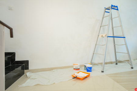 Medium shot of a white wall next to which there is a stepladder, paint cans, brushes and a roller. Concept of renovation in a new apartment before moving. Painters. Banner for renovation work.の写真素材