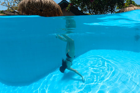 Underwater young woman dives into blue water pool in black bikini and mask. She trains breath...
