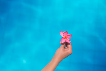 Background banner for spa salon. Hand of a young woman holding a pink plumeria flower against blue...