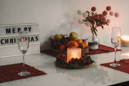 Festive table setting for Christmas dinner. There are red napkins, candles, fruits and champagne...