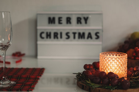 Festive table setting for Christmas dinner. There are red napkins, candles, fruits and champagne glasses on the table. In the background there is a sign with the inscription Merry Christmas.の写真素材