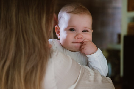 Close-up portrait of a charming infant baby girl being held by her mother. She has big blue eyes and a sweet smile. Health and care of a newborn. Breastfeeding.の写真素材