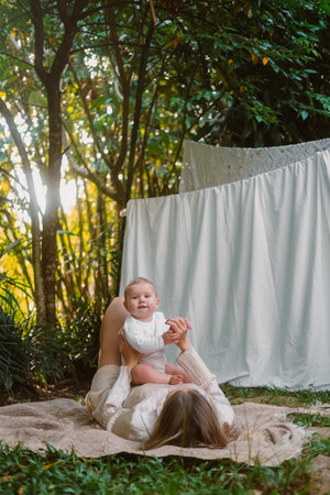 Woman lying on blanket in the garden near the house and holding her infant daughter in arms. They...