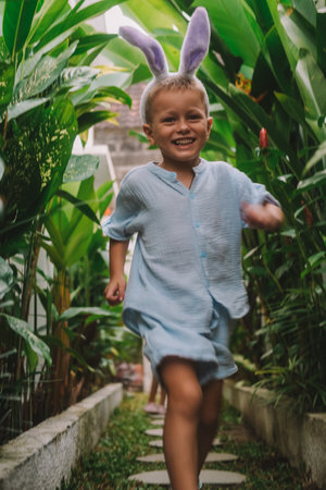 Festive Easter childrens game Egg hunt. The little boy search of eggs, collects them in a basket and...
