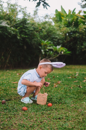 Festive Easter childrens game Egg hunt. The little boy search of eggs, collects them in a basket and has fun against the backdrop of festive decorations. Family traditions.の写真素材