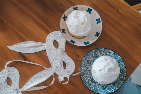 Top down view of a table with two festive Easter cakes with cream and decor. Homemade rabbit masks...