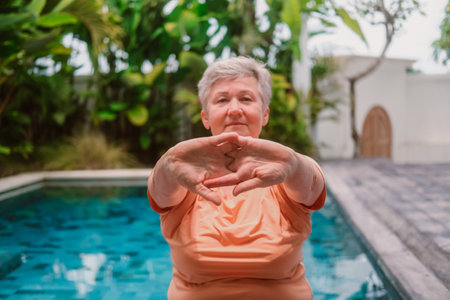 Close-up portrait of a senior woman with gray hair doing therapeutic exercises for her hands in a tropical villa next to a swimming pool. Rest and recovery in retirement.の写真素材
