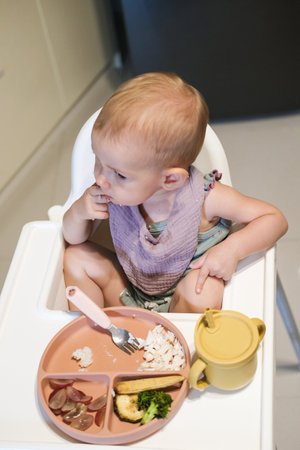 Top view of a high chair for feeding a toddler which stands in the kitchen and a little girl sits behind it eating lunch. Toddler learns to eat independently. Proper nutrition for toddlers.の写真素材