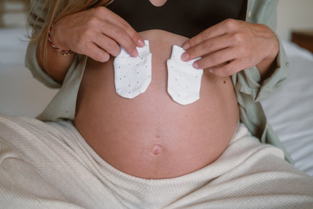 Close up of a pregnant woman big belly, she puts little socks on her belly in anticipation of the...