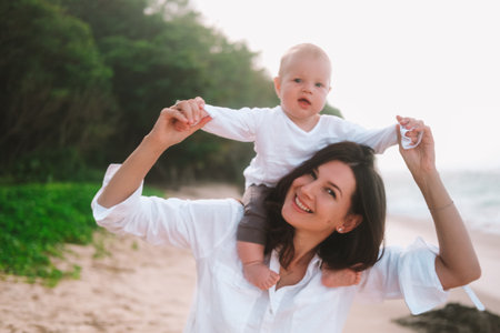 Portrait of mother and child who sits on her neck and laughs. Woman smiling and walking with child...