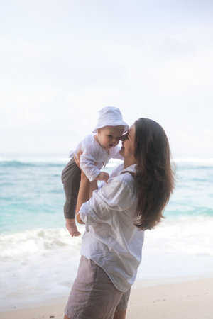 Portrait of a mother who is spinning her baby on the beach and playing with him. Family vacation at sea. Mothers love for her son. Mothers Day.の写真素材