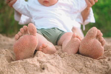 Close up of baby and mothers feet sitting on the beach on the sand and relaxing. Family vacation by the ocean on the beach in the tropics. Baby first steps on the sand. Mothers Day.の写真素材