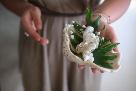 Close up of young womans hands holding shell with silver wedding rings. Outdoor tropical wedding...