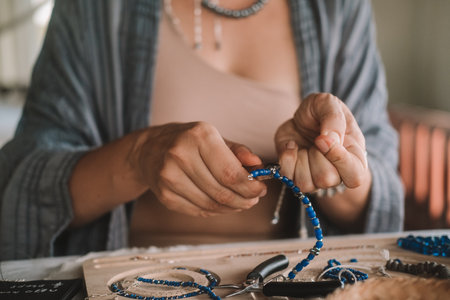 Close up of hands woman jewelry designer. She is sitting at a workspace with tools on it and is...