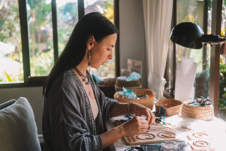 Portrait of a young brunette woman jewelry designer. She is sitting at a work table on which lie...