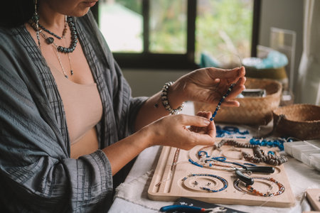Close up of hands woman jewelry designer. She is sitting at a workspace with tools on it and is...