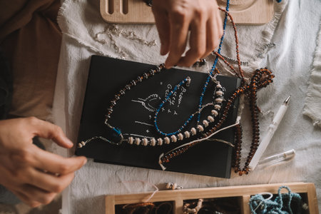 Close up of hands woman jewelry designer. She is sitting at a workspace with tools on it and is...