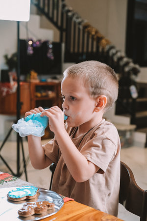 A festive Christmas gingerbread baking workshop for children. Kids are fooling around at the kitchen table and eating icing from a piping bag. A fun activity for kids in the Christmas Eve.の写真素材