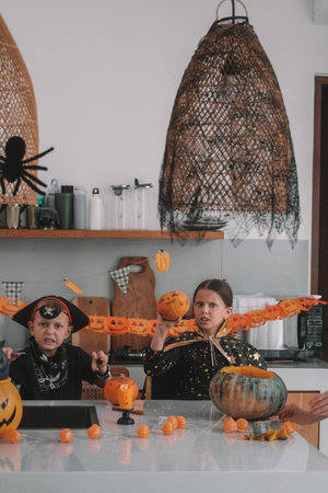 Portrait of a girl and her little brother celebrating Halloween and decorating pumpkins in the...