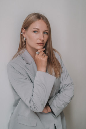 A portrait of a blonde businesswoman in a classic gray jacket standing in an office against a white wall, looking thoughtful.の写真素材