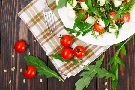 Salad with arugula, cherry tomatoes, mozzarella, quail eggs and pine nuts on a wooden backgroundの写真素材