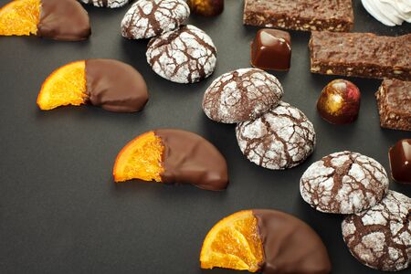 A set of home-made sweets: brownies, marshmallows, cookies, marmalade, delicious slices of orange in chocolate and candies. On a black background. Close-up.の写真素材