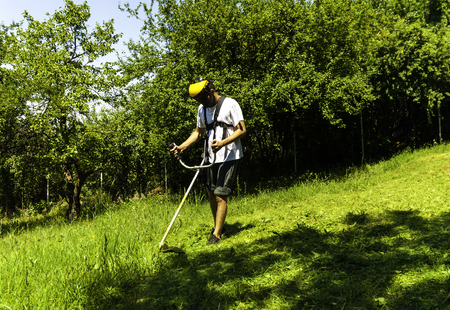 Close up of man mowing green wild grass field using brush cutter mower or power tool string lawn...