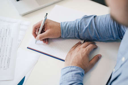 Man holding pen pencil in hand filling writing taking notes into notes starting new chapter...