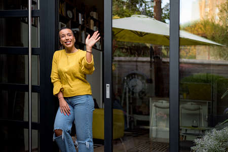 Portrait of casual relaxed woman using phone for online payment on doorstep of her home shopping online from home leaning on door frame using credit card casual entrepreneur doing business from homeの写真素材