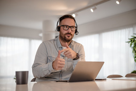 Serious businessman wearing headset and gesturing. Male executive wearing smart casuals is working...
