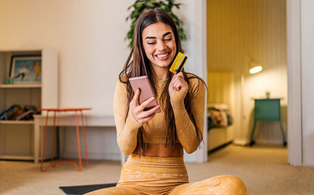 Cheerful brunette woman, using her credit card to buy something online, on her phone.
