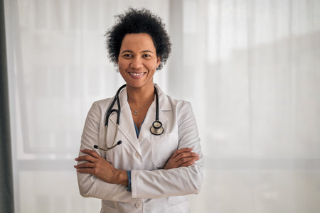 Portrait of confident smiling female healthcare professional, Doctor is standing with arms crossed against window, She is wearing lab coat and stethoscope.の写真素材