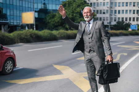 Elderly professional with laptop bag waving for taxi cab in the city.の写真素材