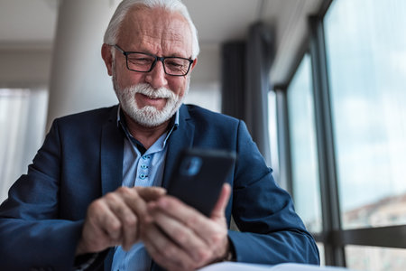 Senior businessman checking using mobile smart phone i modern officeの写真素材