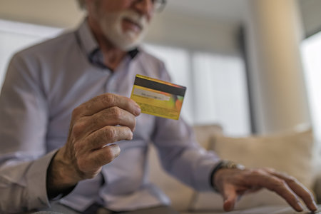 Close-up shot of senior businessman doing online shopping with credit card, Elderly entrepreneur making online payment, he is wearing eyeglasses at office. Focus on credit card and hand.の写真素材