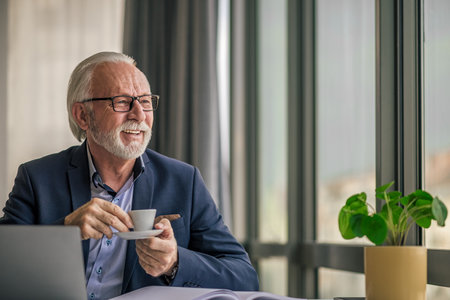 Senior businessman drinking coffee while working on laptop. Elderly male professional is looking...