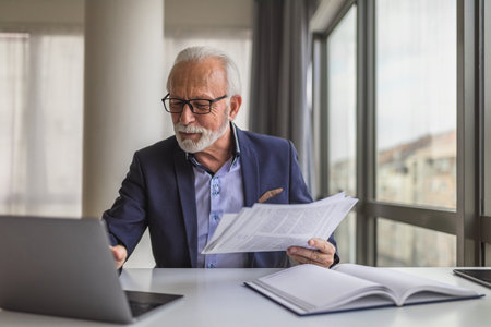 Bearded senior entrepreneur with eyeglasses, checking his work calendar on his laptop, at the...