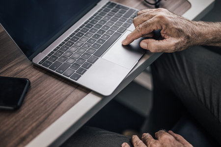 Close-up of senior male professional scrolling on laptop at table. Businessman is working in subway or passenger intercity train. He is using wireless technology during business travel.の写真素材