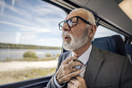 Close-up of stressed senior businessman feeling uncomfortable while traveling on the train having a heart attack.の写真素材