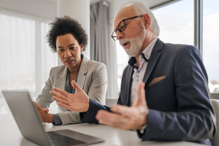 Confident male and female professionals brainstorming over laptop. Business executives discussing during meeting. They are sitting at desk while working in corporate office.の写真素材