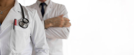 Male and female healthcare professionals against white background, Midsection of female doctor with stethoscope, They are wearing lab coats.の写真素材