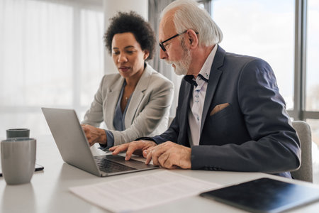 Confident business partners discussing while working on laptop. Male and female colleagues planning strategy during meeting. They are working at desk in office.の写真素材