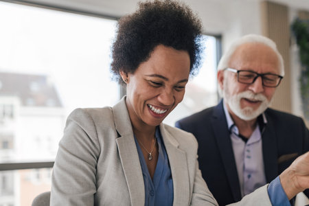 Multiracial woman laughing at funny joke with diverse senior male coworker in office. Friendly work team looking at documents and enjoying positive emotions together. Happy colleagues conceptの写真素材