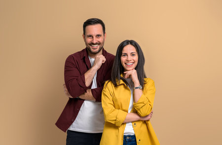 Charming young man and woman with hands on chins smiling and looking at camera. Confident joyful boyfriend and girlfriend wearing casuals and posing over beige backgroundの写真素材
