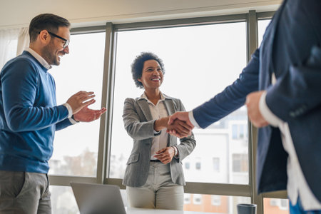Smiling african american woman, handshaking with her colleague, while her male coworker claps.の写真素材