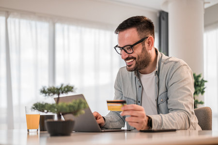 Cheerful professional making online payment with credit card. Businessman working on laptop at desk. He is wearing business casuals at office.の写真素材