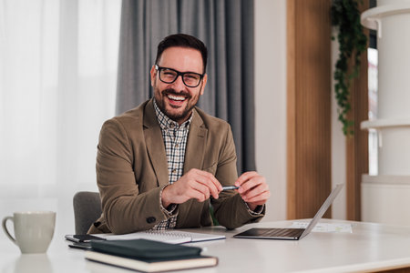 Portrait of confident smiling entrepreneur with laptop and diary. Young businessman is sitting at desk in office. He is wearing formals in workplace.の写真素材